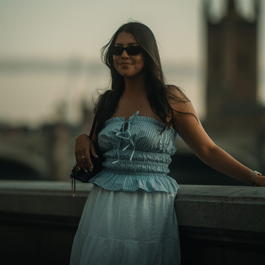 Woman in a blue dress standing by a railing with a blurred background