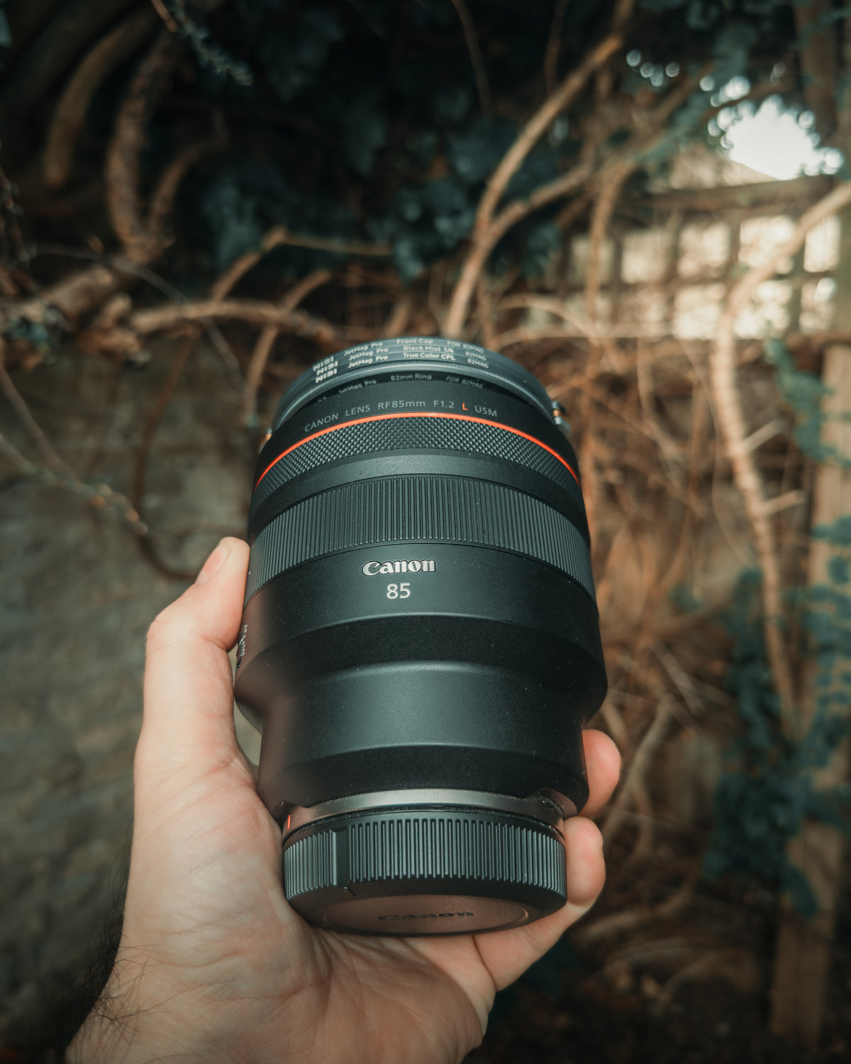 A Canon RF 85mm f/1.2L lens held in one hand